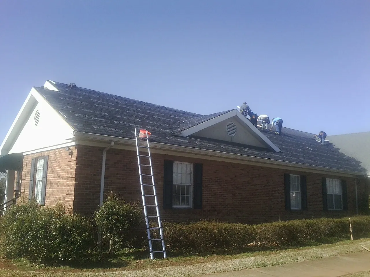 Crew tearing shingles off a brick ranch roof with a ladder set — Metal Roof Repair work by our crew in Armuchee