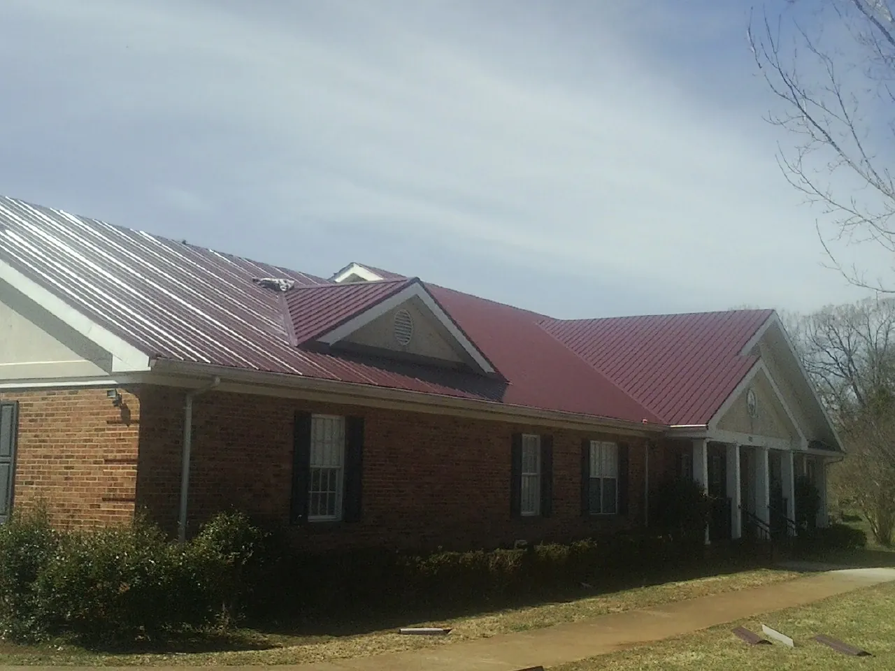 Red metal roof with gabled entries on a long brick building, from a Hail Damage Roof Repair job in Armuchee