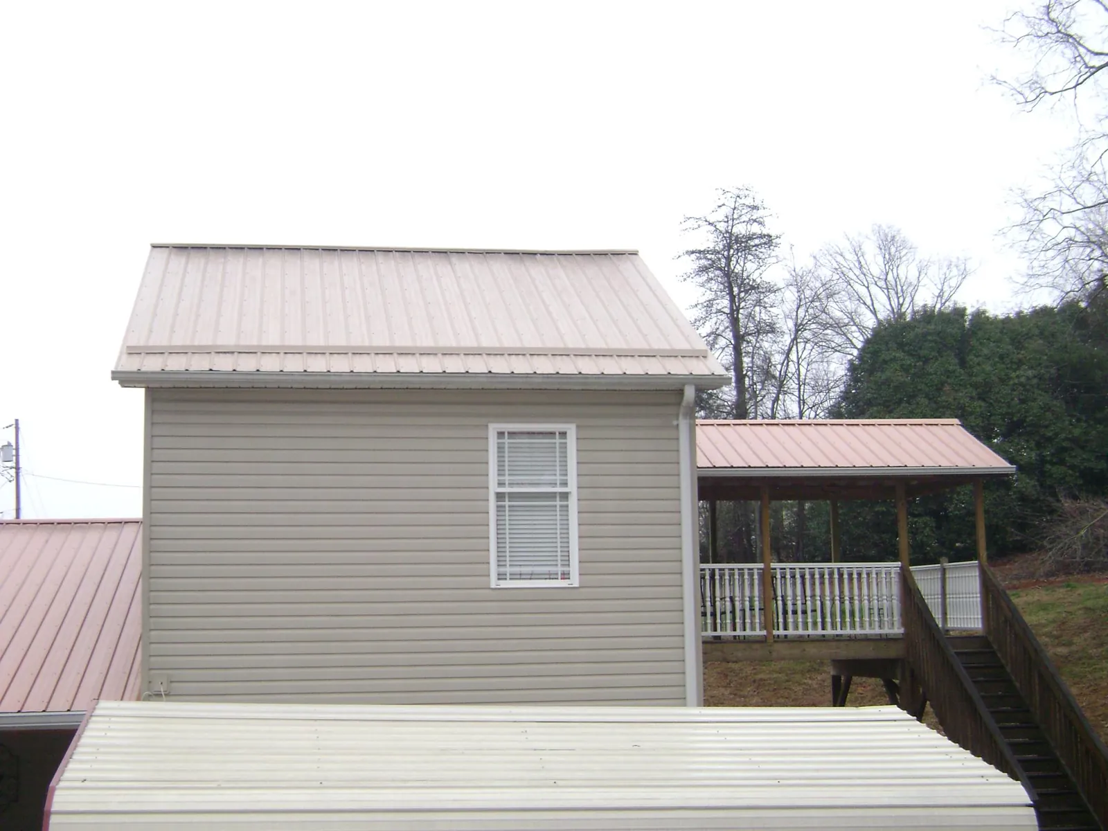 Tan metal roofs on a two story addition and attached porch, from a Roof Replacement job in Armuchee
